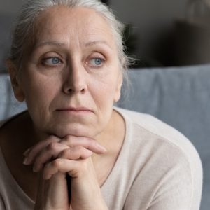 Head shot of older adult woman looking out into the distance, look of worry and stress on her face