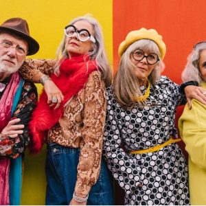 Group of four older adults feeling confident and youthful in colourful clothing standing together against a colorful wall