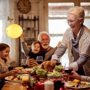 Happy mature woman serving Holiday meal to family at dining table