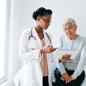 black female doctor standing next to female patient showing her something on digital tablet