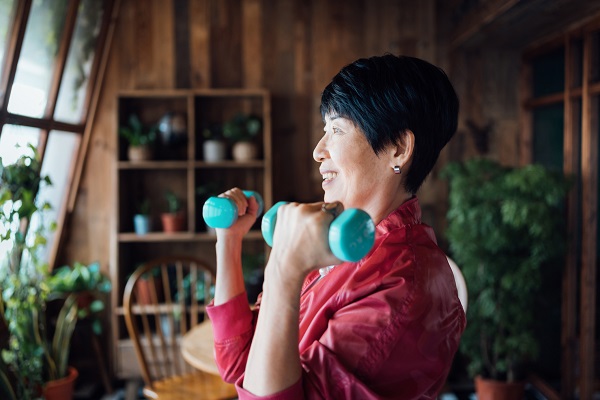 Active senior Asian woman exercising at home. Practicing fitness training and lifting dumbbells. Maintaining healthy fitness habits. Elderly wellbeing, health and wellness concepts