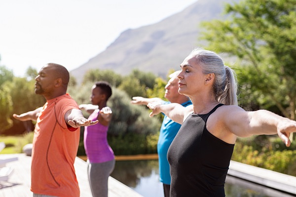 Group of senior people with closed eyes stretching arms outdoor. Happy mature people doing breathing exercise near pool. Yoga class with women and men doing breath exercise with outstretched arms. Balance and meditation concept.